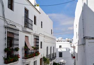 Edificios blancos con balcones y flores en una calle estrecha de TAIGA Conil, Andalucía, España.