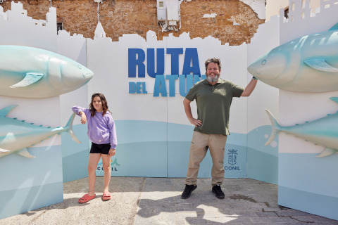 Hombre y niña posan frente al cartel 'Ruta del Atún' con grandes figuras de atún en TAIGA Conil, Andalucía, España.