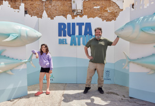 Man en meisje poseren voor het bord 'Ruta del Atún' met grote tonijnbeelden in TAIGA Conil, Andalusië, Spanje.