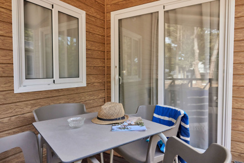 Mesa y sillas en la terraza del Bungalow Confort Poniente en TAIGA Conil, España, con sombrero y toalla.