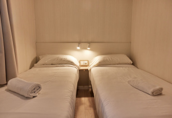 Dos camas individuales con sábanas blancas en Bungalow Confort Poniente, TAIGA Conil, España, con toallas listas.