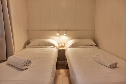 Dos camas individuales con sábanas blancas en Bungalow Confort Poniente, TAIGA Conil, España, con toallas listas.