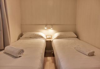 Dos camas individuales con sábanas blancas en Bungalow Confort Poniente, TAIGA Conil, España, con toallas listas.