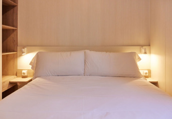 Soveværelse med dobbeltseng og hvidt sengetøj i Bungalow Confort Poniente, TAIGA Conil, Spanien.