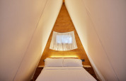 Gemütliches Schlafzimmer im Glamping Tipi Pinar Chalet bei TAIGA Conil, Spanien mit Holzwänden.
