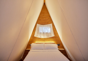 Acogedor dormitorio interior del Glamping Tipi Pinar en TAIGA Conil, España, con diseño triangular.