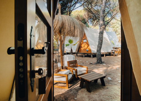 Udsigt fra en dør til hyggelige glamping tipi-chaletter og loungemøbler hos TAIGA Conil i Spanien.