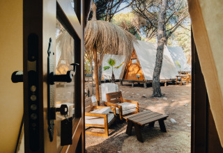 Udsigt fra en dør til hyggelige glamping tipi-chaletter og loungemøbler hos TAIGA Conil i Spanien.