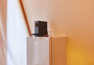 Ein kleiner Kühlschrank mit Kaffeemaschine auf einem hölzernen Ständer im Glamping Tipi Pinar, TAIGA Conil, Spanien.