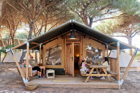 Familia relajándose frente a una tienda safari glamping en TAIGA Conil, España, con dos niños en la mesa.