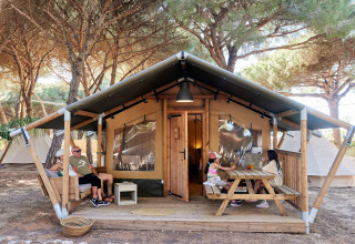 Familia relajándose frente a una tienda safari glamping en TAIGA Conil, España, con dos niños en la mesa.