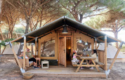 Familia relajándose frente a una tienda safari glamping en TAIGA Conil, España, con dos niños en la mesa.