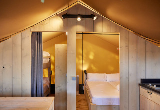 Vista interior de una tienda glamping Safari con cama doble y litera en TAIGA Conil, España.