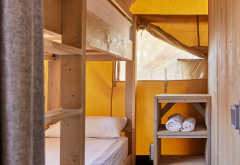 Intérieur d'une tente safari avec lits superposés en bois, étagère et serviettes roulées, ambiance chaleureuse.