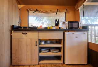 Cocina completamente equipada en una tienda safari con nevera, microondas y estantes en TAIGA Conil, España.