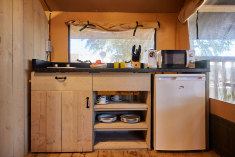 Fully equipped kitchenette in a safari tent with fridge, microwave, and wooden shelves at TAIGA Conil, Spain.