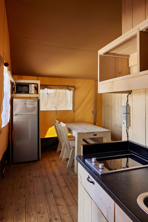 Interior de la tienda Glamping Safari Siroco Premium en TAIGA Conil, España, con cocina y zona de comedor.