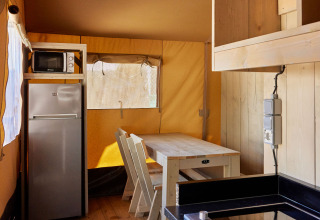 Interior de la tienda Glamping Safari Siroco Premium en TAIGA Conil, España, con cocina y zona de comedor.