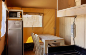 Interior de la tienda Glamping Safari Siroco Premium en TAIGA Conil, España, con cocina y zona de comedor.