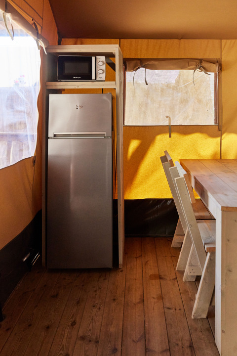 Zona de cocina en Glamping Safari Siroco Premium con nevera, microondas y mesa de comedor en TAIGA Conil, España.