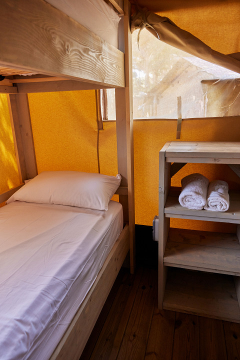 Vista interior de una tienda Glamping Safari Siroco Premium con litera y toallas sobre un estante de madera.