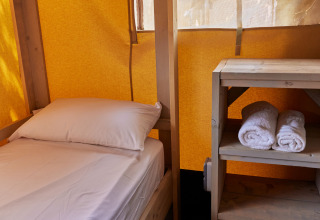 Vista interior de una tienda Glamping Safari Siroco Premium con litera y toallas sobre un estante de madera.