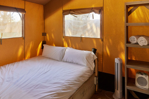 Interior de una tienda Glamping Safari Siroco Premium en TAIGA Conil, España, con cama y estantería.