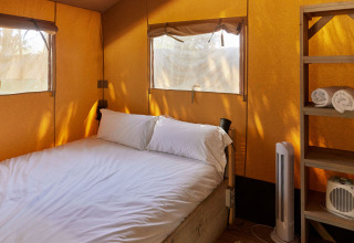 Interior de una tienda Glamping Safari Siroco Premium en TAIGA Conil, España, con cama y estantería.
