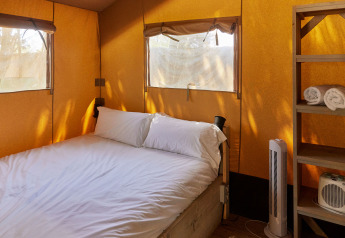 Intérieur d'une tente Glamping Safari Siroco Premium à TAIGA Conil en Espagne, avec lit et étagère en bois.