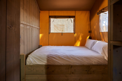 Foto del interior de una cama acogedora con sábanas blancas en la tienda Glamping Safari Siroco Premium en España.