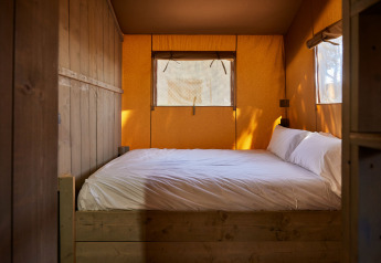 Foto interna di un letto accogliente con lenzuola bianche nella tenda Glamping Safari Siroco Premium in Spagna.