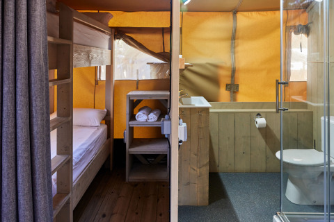Vista interior de la tienda Glamping Safari Siroco Premium en TAIGA Conil, España, con literas y baño moderno.