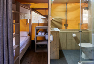 Vista interior de la tienda Glamping Safari Siroco Premium en TAIGA Conil, España, con literas y baño moderno.