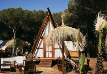 Glamping Tipi Almadraba à TAIGA Conil en Espagne avec tente tipi en bois, sièges extérieurs et toit en paille.