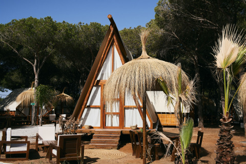 Glamping Tipi Almadraba al TAIGA Conil, Spagna, con tenda tipi in legno, sedute all’aperto e parasole di paglia.