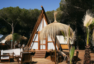 Glamping Tipi Almadraba al TAIGA Conil, Spagna, con tenda tipi in legno, sedute all’aperto e parasole di paglia.