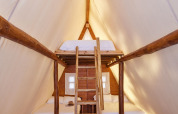 Intérieur du Glamping Tipi Almadraba à TAIGA Conil en Espagne, avec mezzanine et lit confortable.