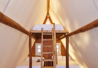 Interior del Glamping Tipi Almadraba en TAIGA Conil, España, con cama en altillo y ambiente acogedor.
