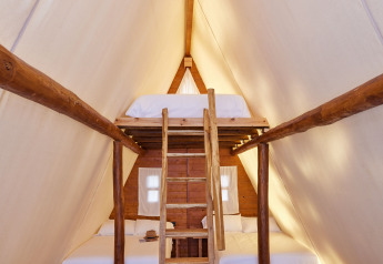 Intérieur du Glamping Tipi Almadraba à TAIGA Conil en Espagne, avec mezzanine et lit confortable.