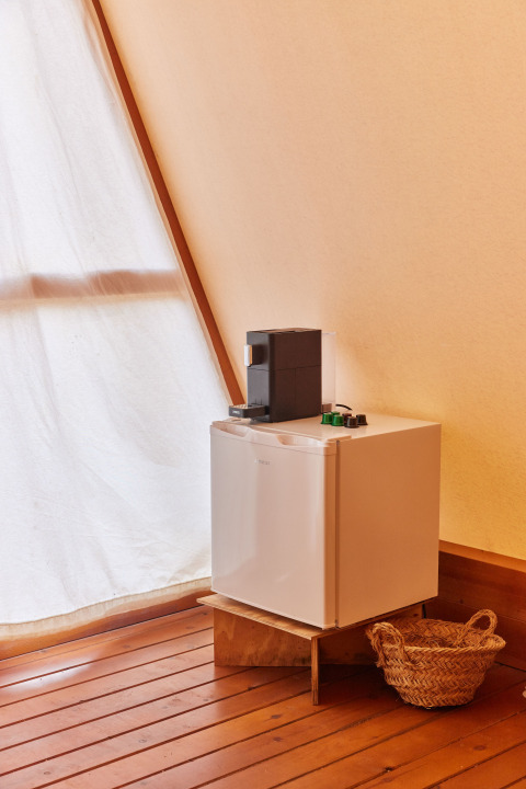 Nevera pequeña con cafetera encima y cesta de mimbre en el suelo de madera en Glamping Tipi Almadraba, España.