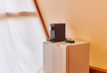 Mini frigo con macchina da caffè sopra e cesta di vimini sul pavimento in legno in Glamping Tipi Almadraba, Spagna.