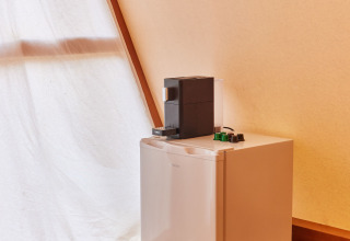 Mini frigo con macchina da caffè sopra e cesta di vimini sul pavimento in legno in Glamping Tipi Almadraba, Spagna.