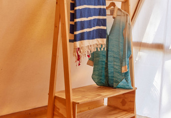 Scaffale di legno con vestiti e asciugamano nel Glamping Tipi Almadraba a TAIGA Conil, Spagna, illuminato.