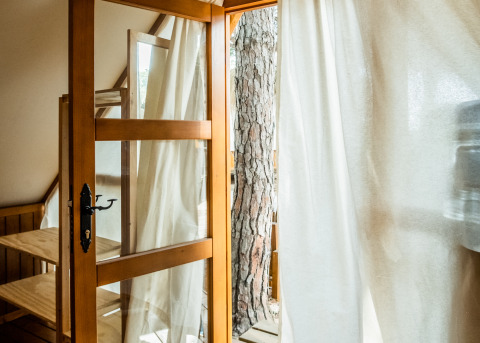 Vista interior de la tienda Glamping Tipi Retama con puerta de madera y cortina blanca en TAIGA Conil, España.