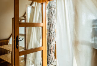 Vista interior de la tienda Glamping Tipi Retama con puerta de madera y cortina blanca en TAIGA Conil, España.