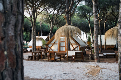 Glamping Tipi Retama safari-telte blandt træer med siddeområder på TAIGA Conil, Spanien, en rolig udendørs oplevelse.
