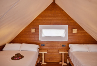 Interior del Glamping Tipi Retama en TAIGA Conil, España, con dos camas y decoración en madera.