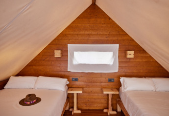 Binnenzicht van Glamping Tipi Retama in TAIGA Conil, Spanje, met twee bedden en houten afwerking.