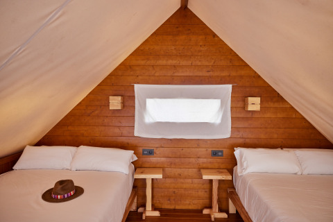 Innenaufnahme des Glamping Tipi Retama, TAIGA Conil, Spanien, mit zwei Betten und Holzverkleidung.