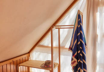 Lumière du soleil dans un coin douillet de la tente Glamping Tipi Retama à TAIGA Conil, avec étagère bois.